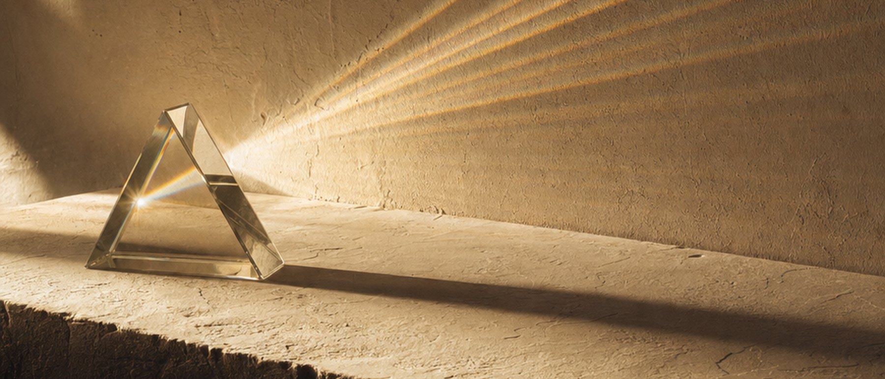 A beam of warm apricot light refracting through a glass prism into fine radiating rays