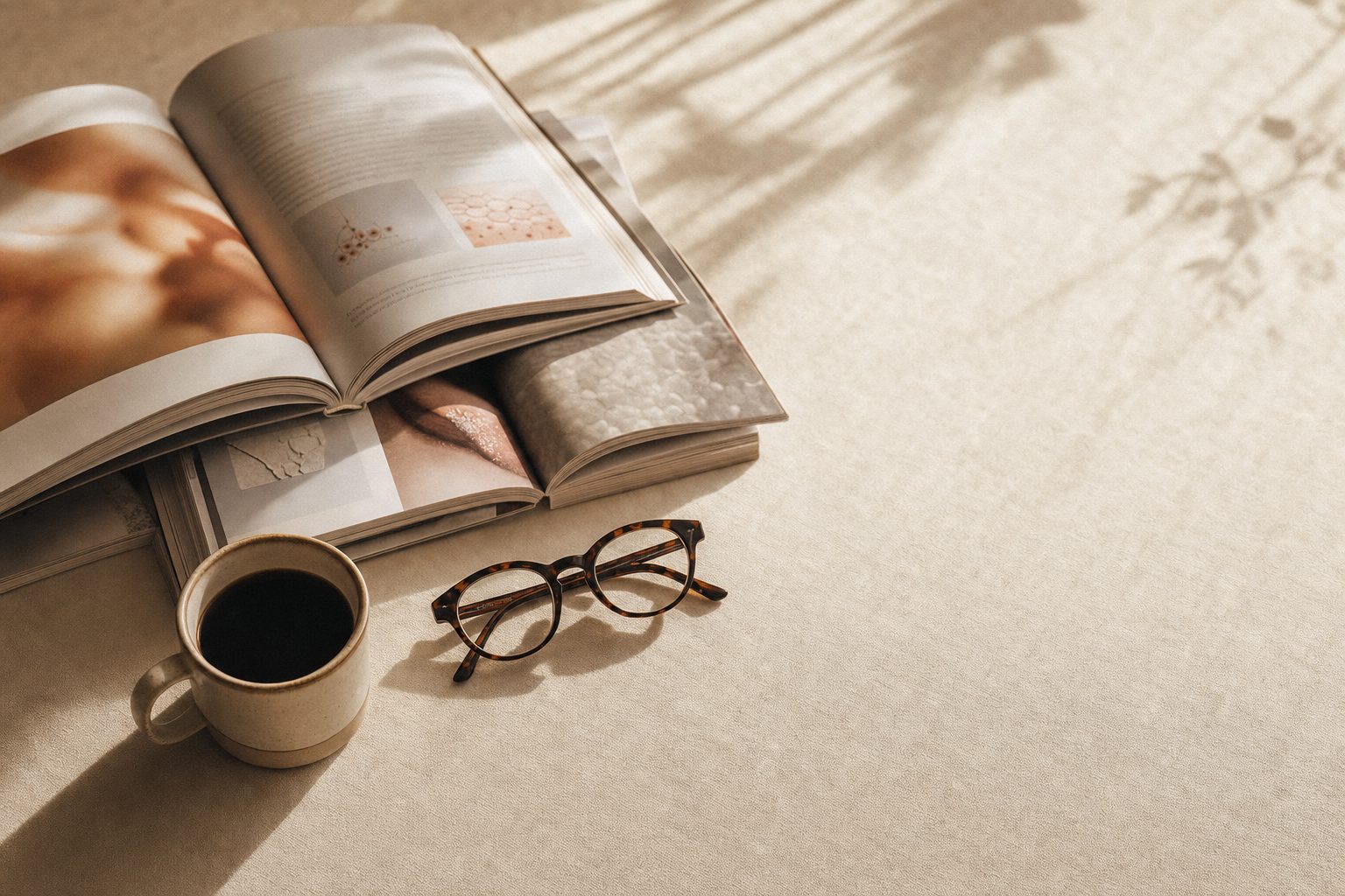 Open journals, tortoiseshell reading glasses and coffee on warm ivory linen